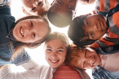 Image of a group of children in a circle looking down at the camera and smiling